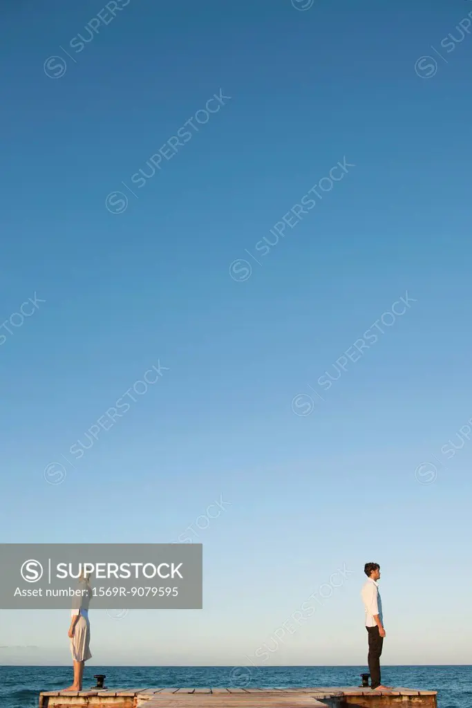 Couple standing back to back on pier, side view