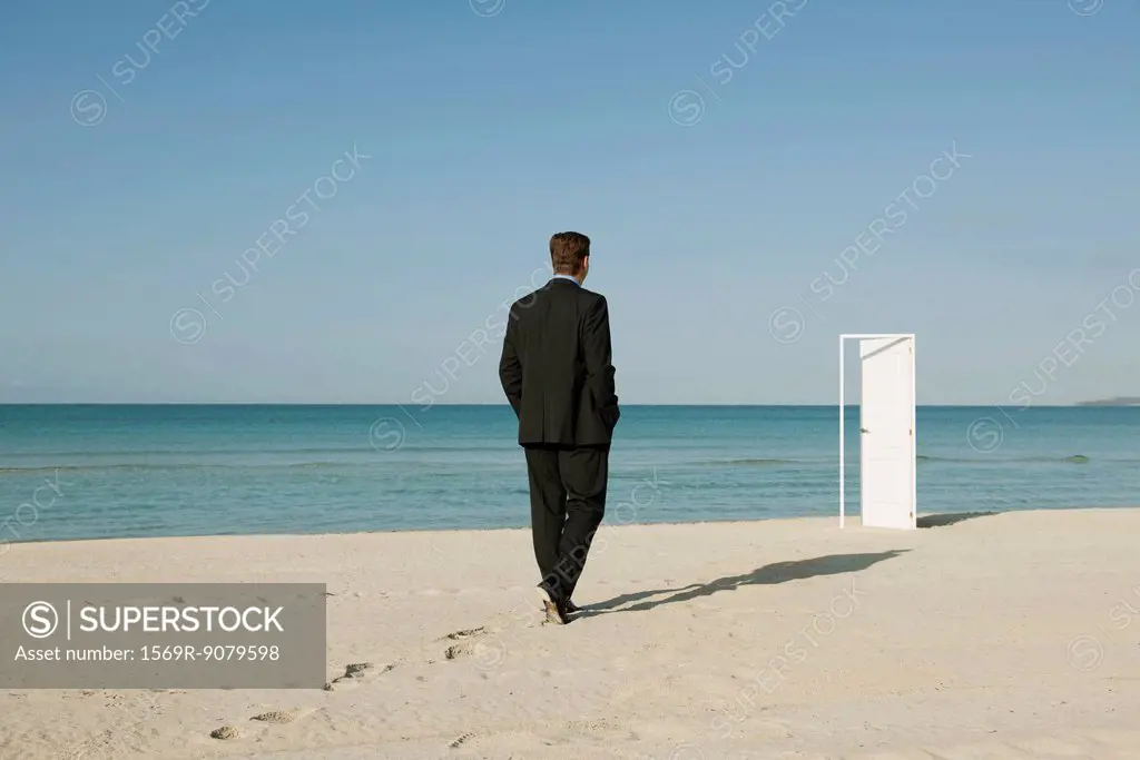 Businessman walking on beach towards half_open door in background