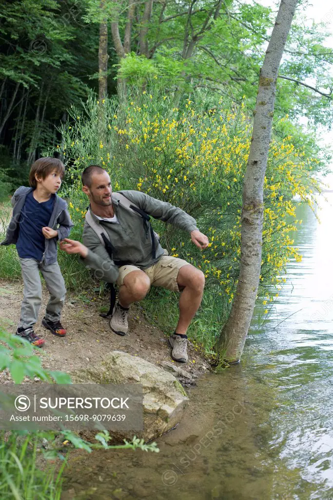 Father and son throwing pebbles into river