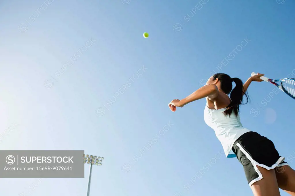 Female tennis player serving ball, low angle view