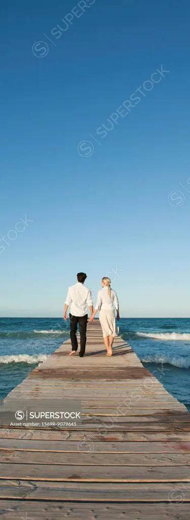 Couple walking on pier holding hands, rear view
