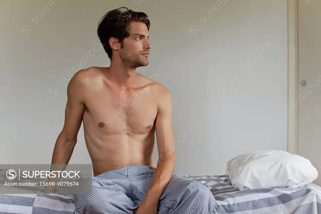 Man sitting on bed, looking away in thought