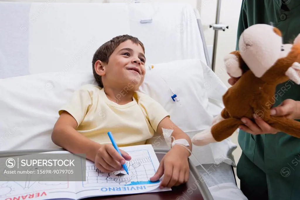 Nurse giving sick boy stuffed animal in hospital, cropped