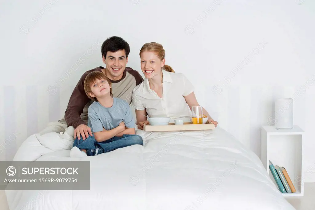 Young family sitting in bed, mother holding breakfast tray