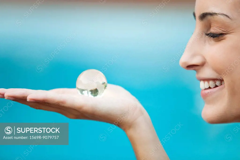 Young woman holding crystal globe in palm, side view