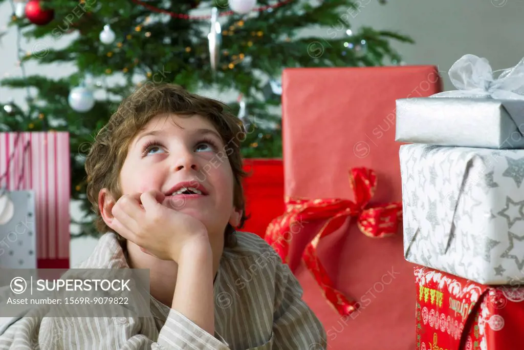 Boy lying beside Christmas presents, daydreaming
