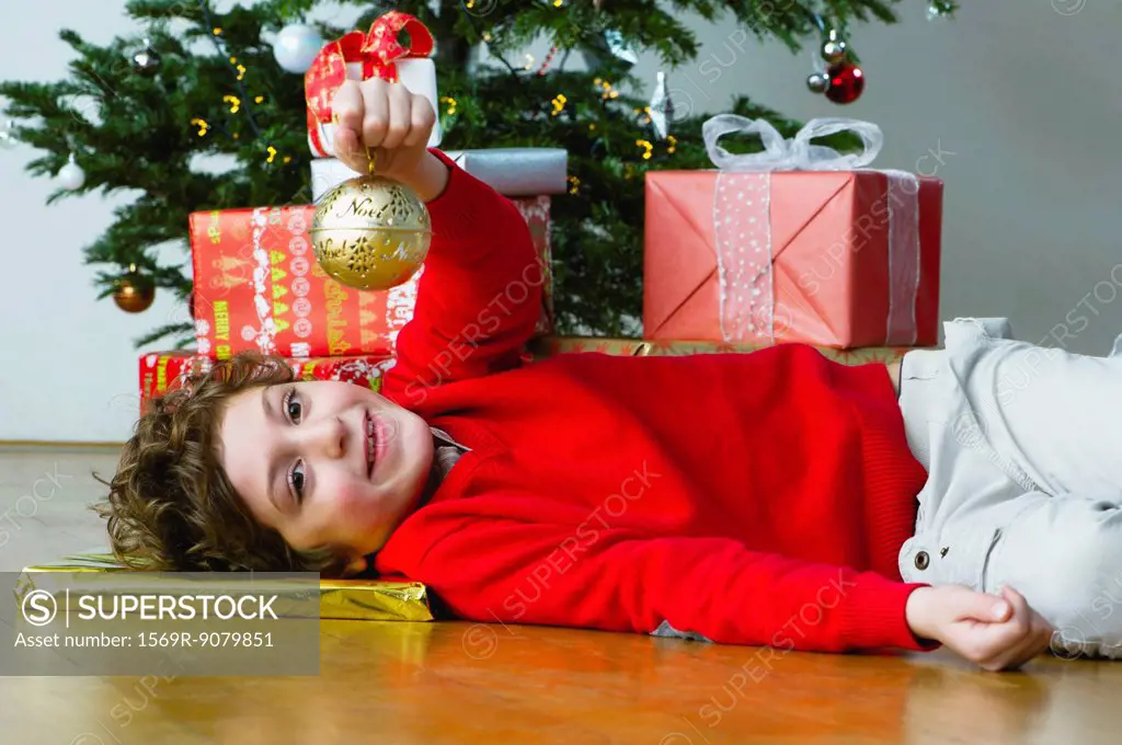 Boy lying on floor by Christmas tree, holding up ornament
