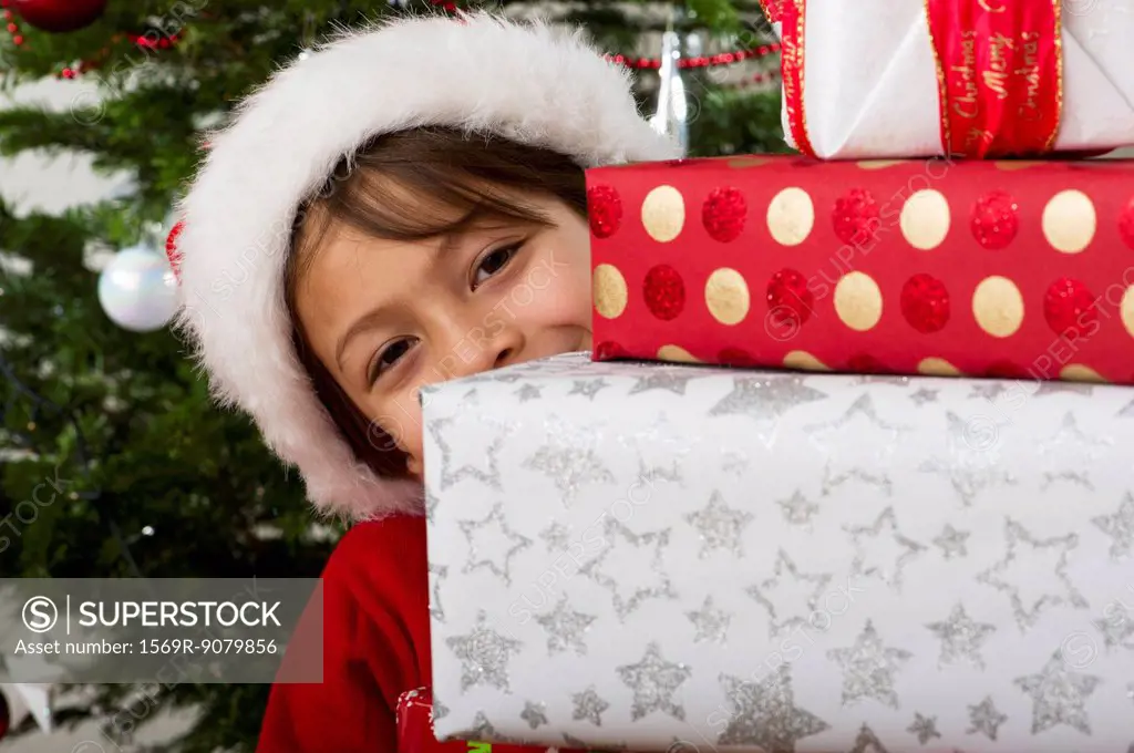 Boy peeking around stack of Christmas presents