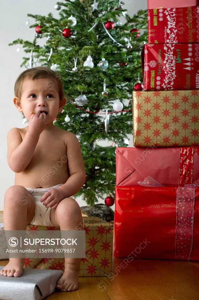 Baby girl sitting on Christmas present, eating snack