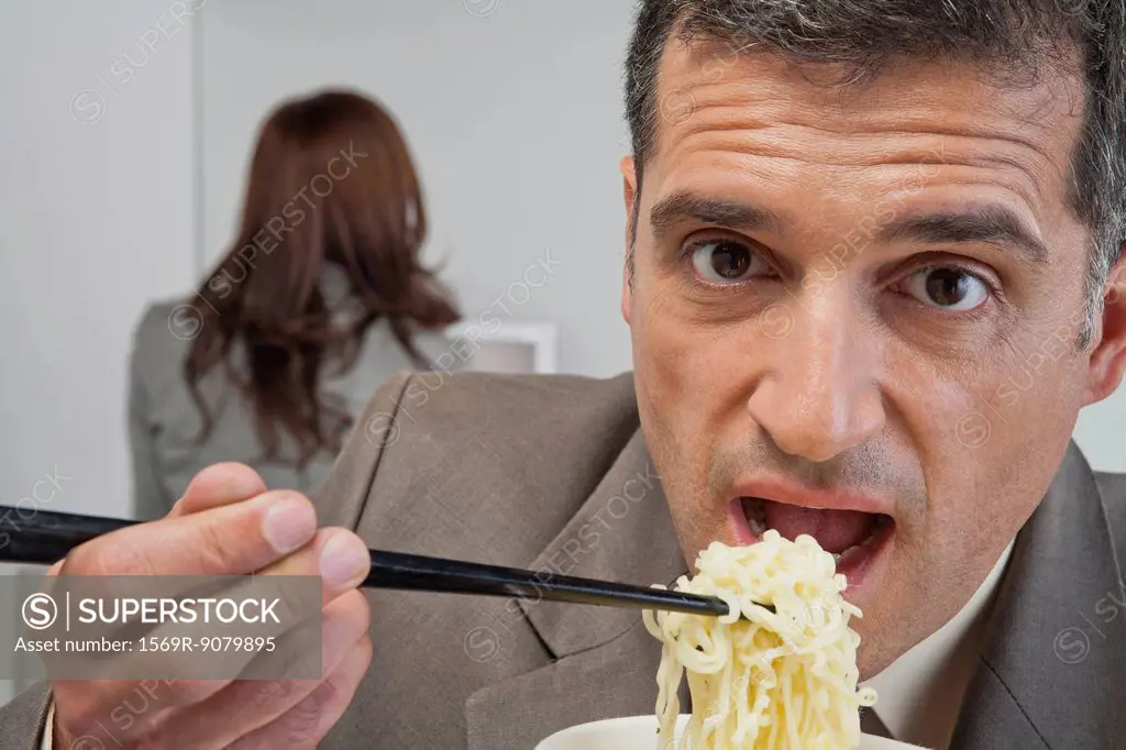 Mature businessman eating ramen noodles in office