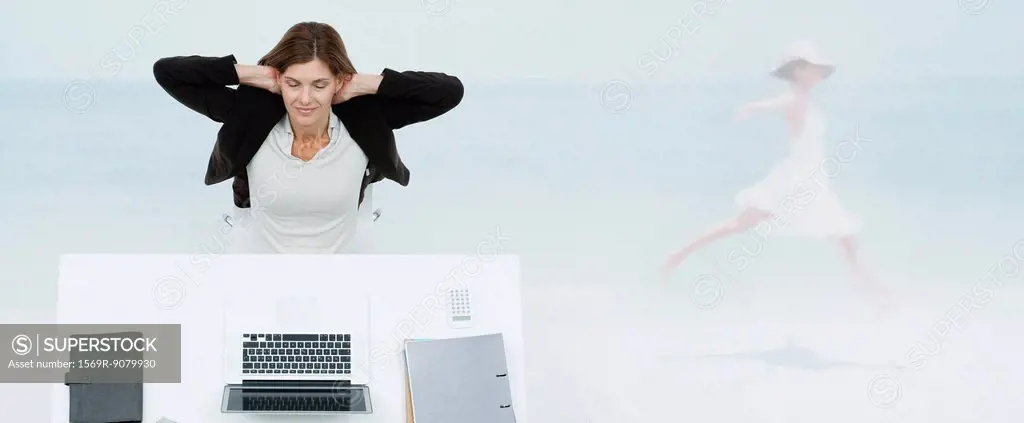Mature businesswoman sitting at desk, imagining herself at the beach