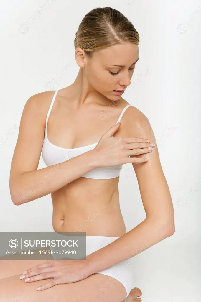 Young woman kneeling in underwear, applying moisturizer to shoulder