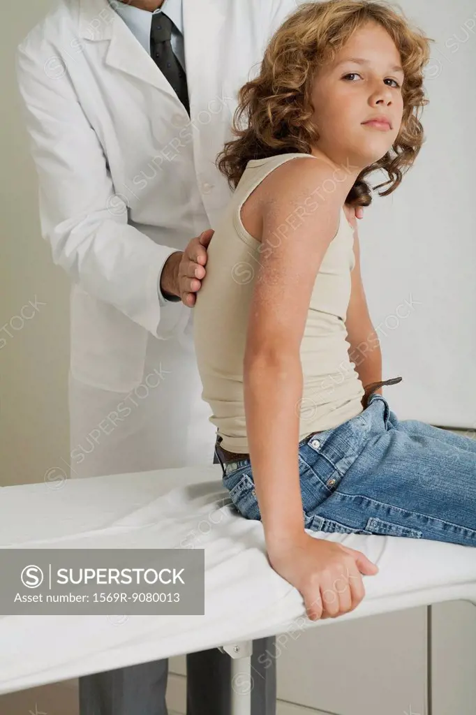 Boy sitting on examination table, doctor examining his back
