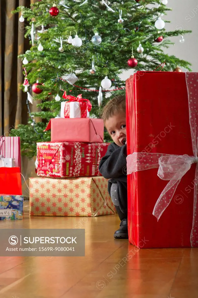 Baby girl hiding behind Christmas present