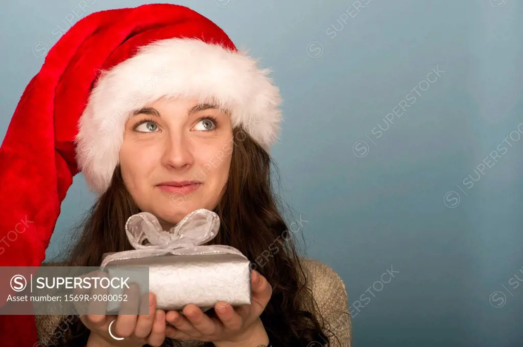 Young woman holding Christmas present, looking up in thought