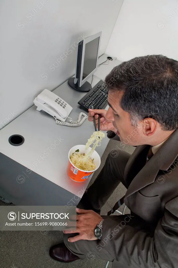 Businessman eating ramen noodles at desk in office
