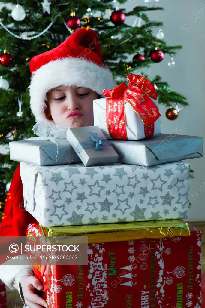 Boy holding stack of Christmas presents with sulky expression on face