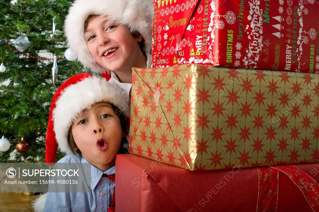Boys peeking around stack of Christmas presents