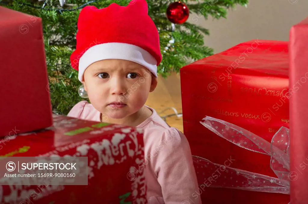 Baby girl sitting by Christmas presents with sulky expression on face