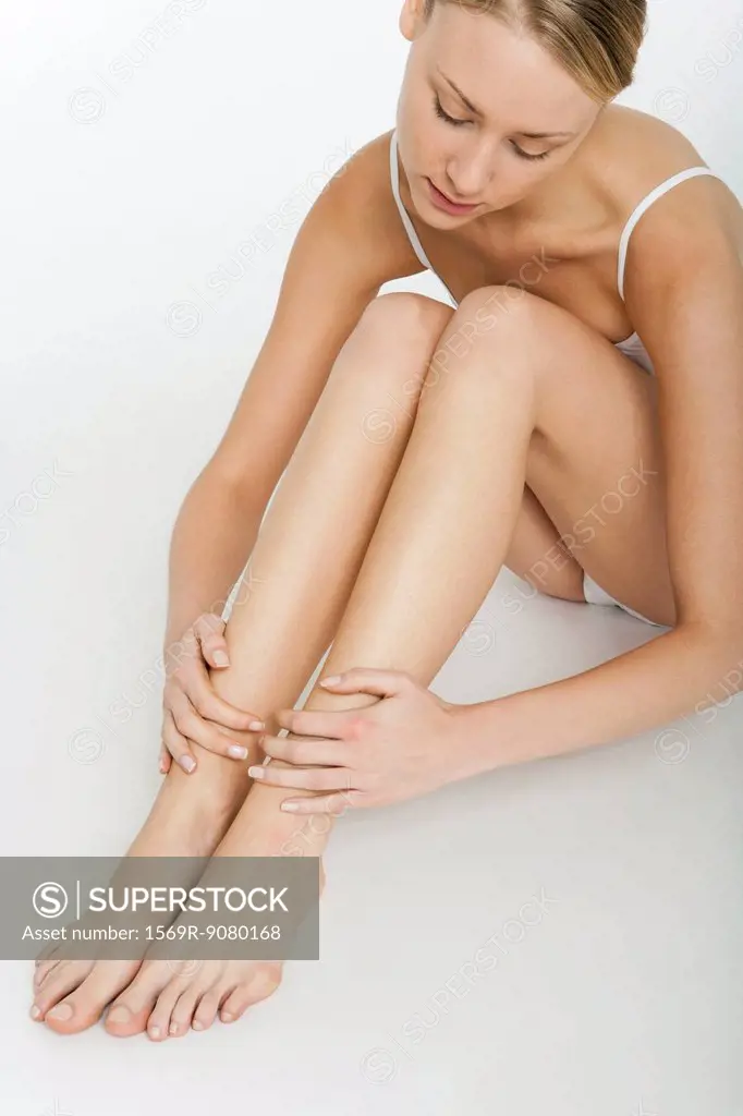 Young woman sitting on floor in underwear, touching bare legs