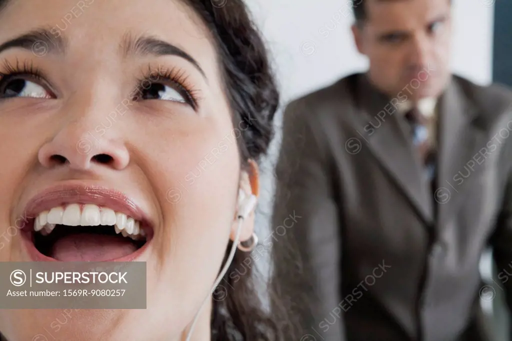 Woman listening to earphones and singing in office, angry boss in background