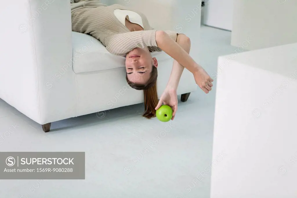 Woman lying upside down on sofa, holding apple