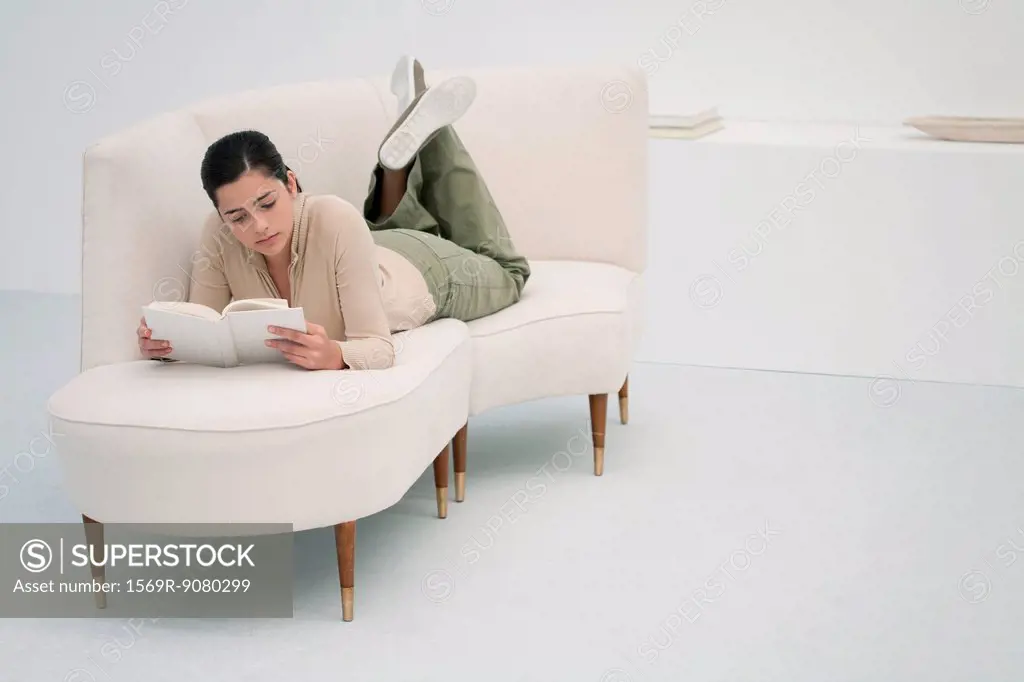 Young woman lying on chaise longue, reading book