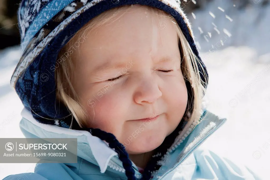 Toddler girl wearing winter clothes in snow with eyes closed, portrait