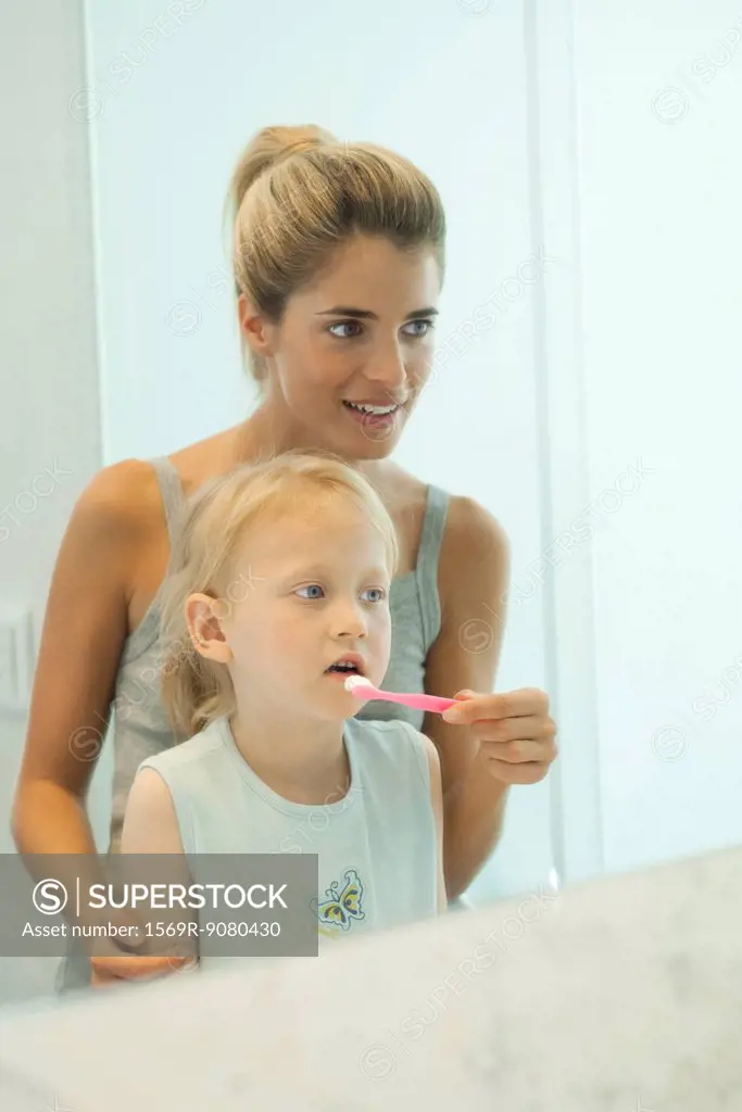 Mother helping daughter brush her teeth