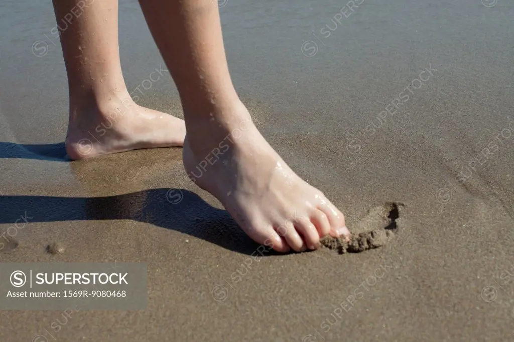 Child drawing in wet sand with foot, cropped