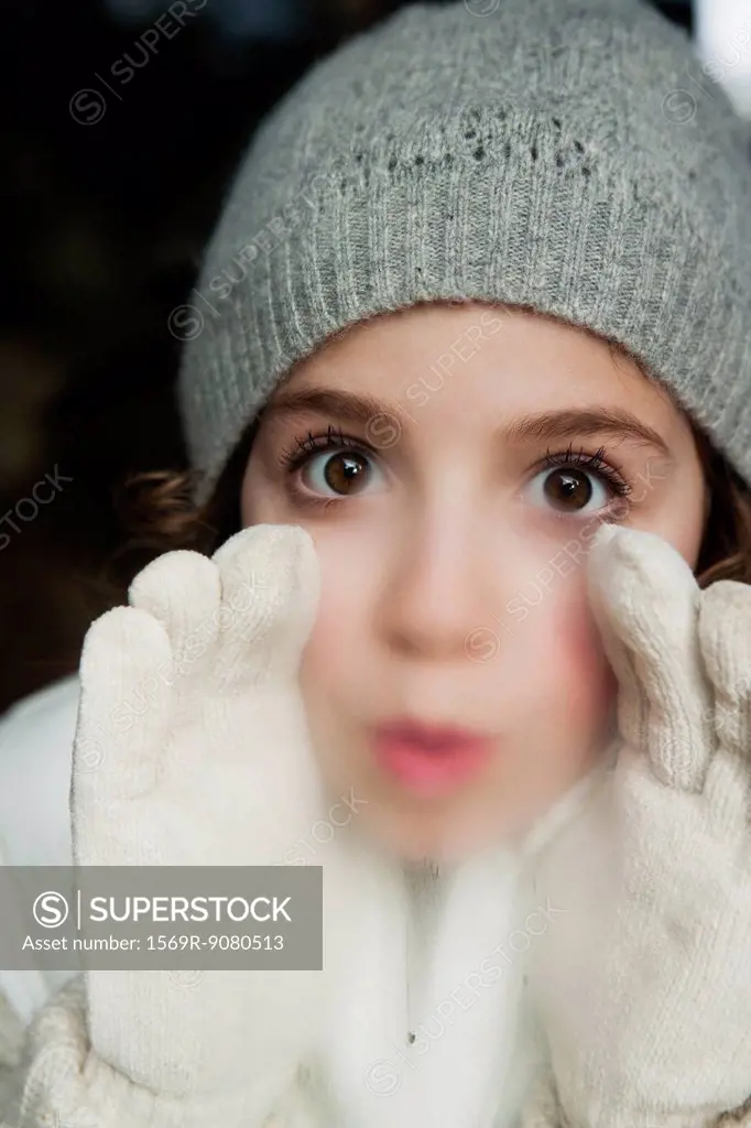 Girl breathing on window, dressed in winter clothes