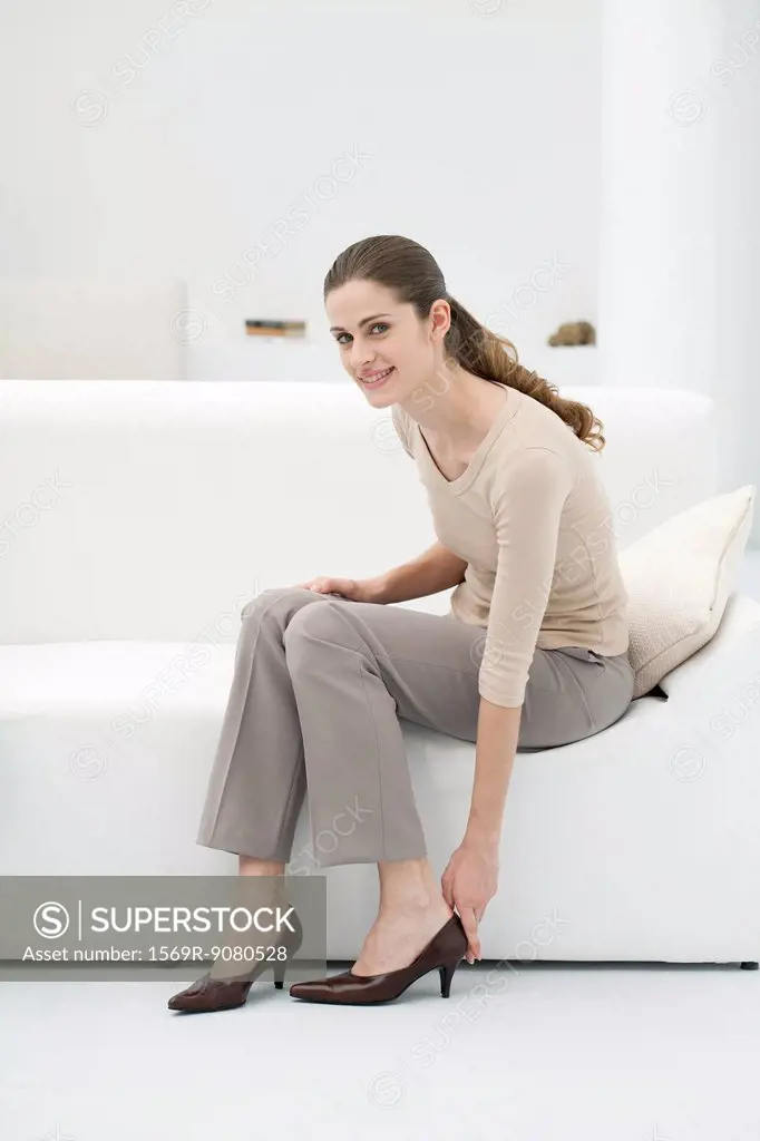 Woman sitting on sofa, putting on high heel shoes