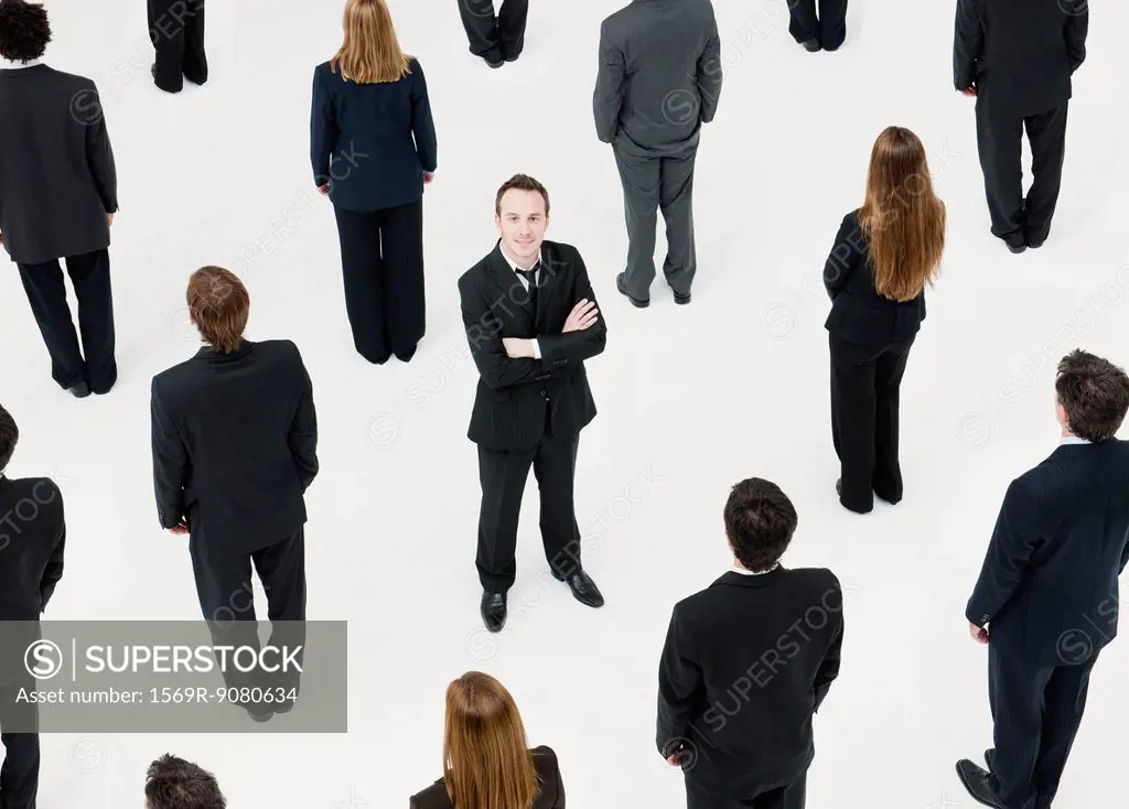 Businessman with arms crossed standing in midst of anonymously dressed business professionals
