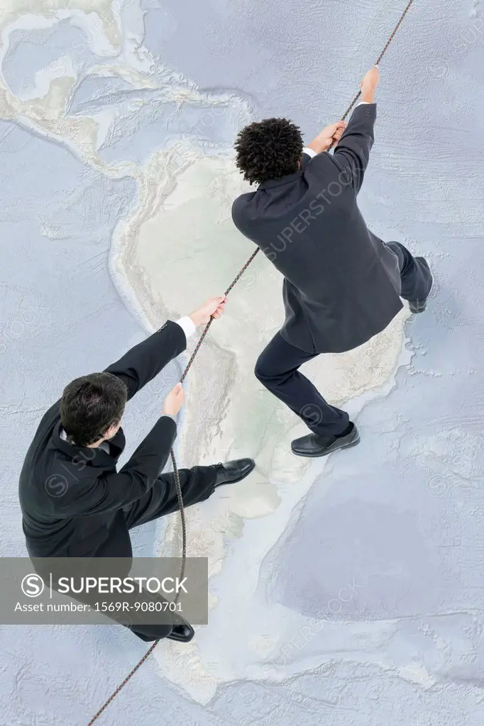 Businessmen standing on top of world map, pulling rope