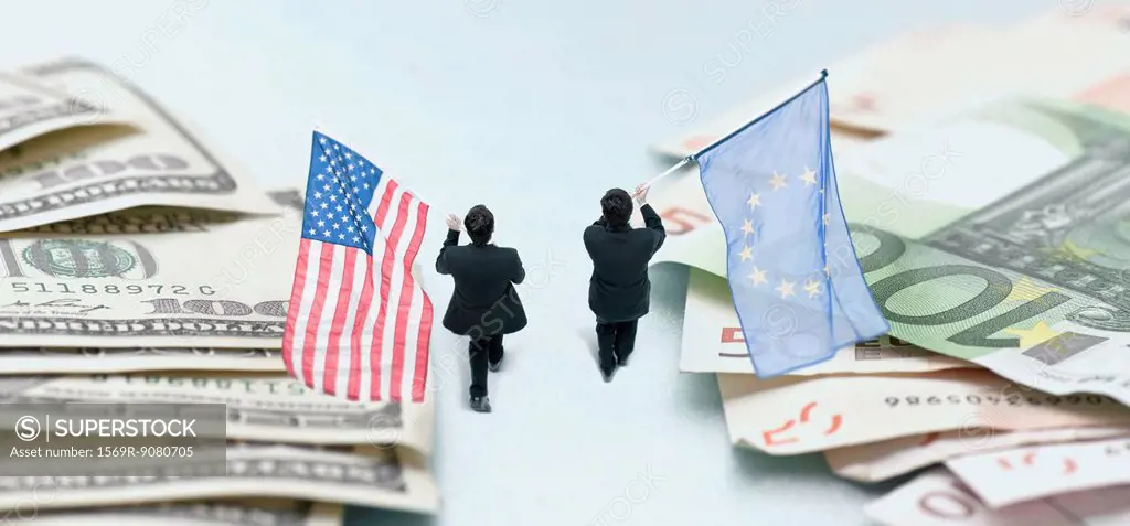 Businessmen marching between piles of money, carrying American and European Union flags