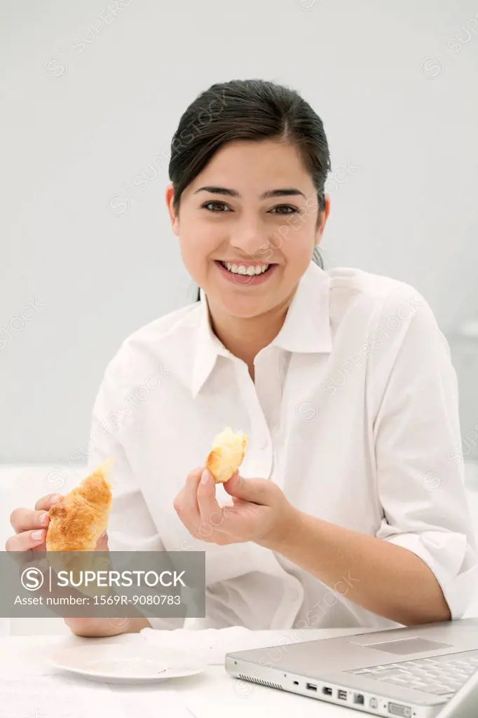 Young woman eating croissant, smiling