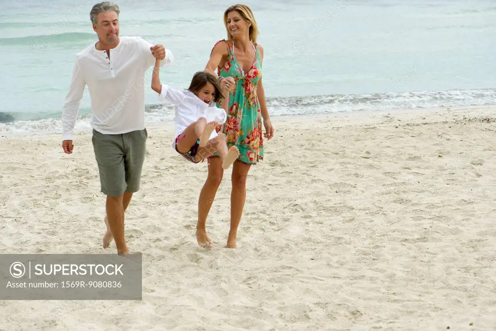 Parents swinging young daughter as they walk on beach