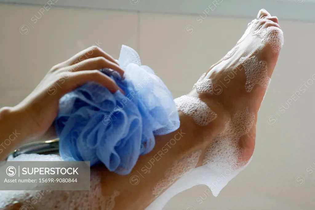 Woman washing foot with bath sponge, cropped