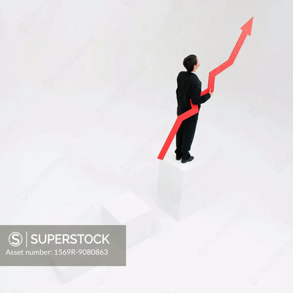 Businessman standing at top of steps holding arrow pointed upward