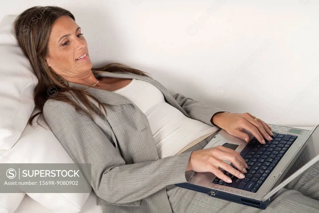 Mature businesswoman lying on couch typing on laptop computer