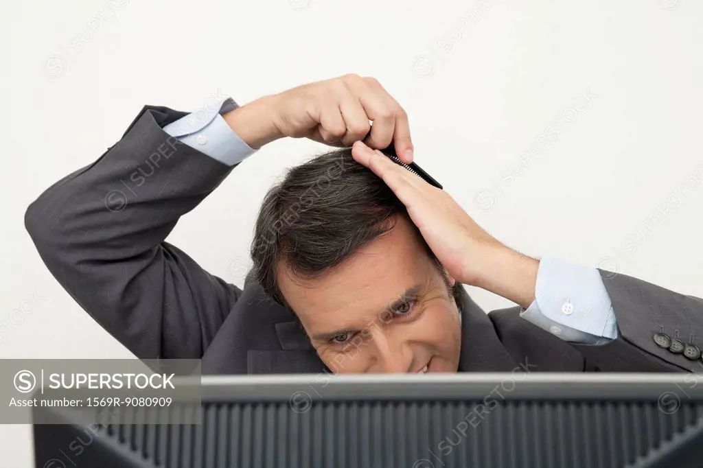 Mature businessman combing hair at desk