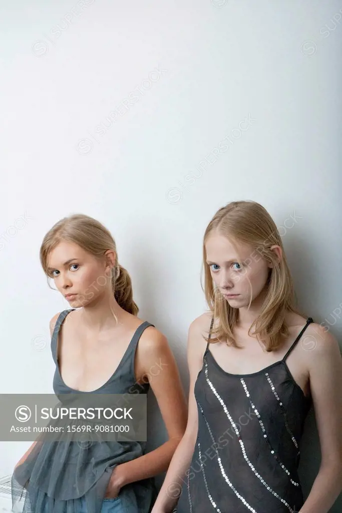 Young woman and teenage girl leaning against wall, looking warily at camera