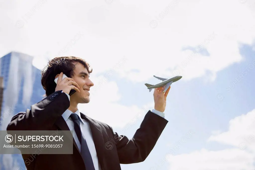 Young executive holding toy airplane while talking on cell phone