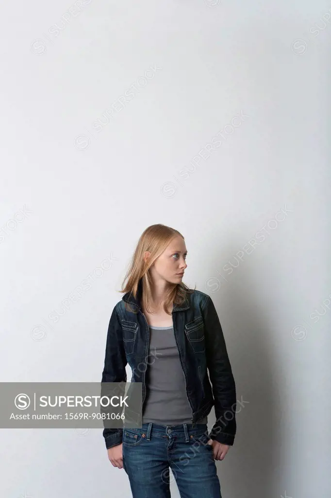 Young woman standing with hands in pockets, looking away