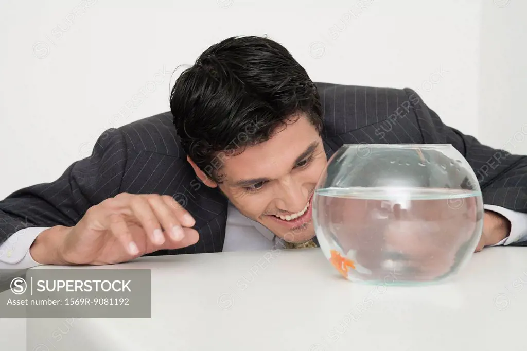 Businessman looking at goldfish in fishbowl, smiling