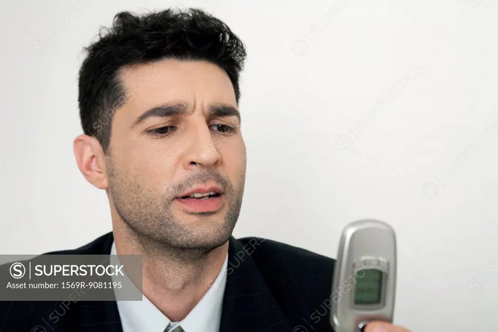Mid-adult businessman looking at cell phone, frowning