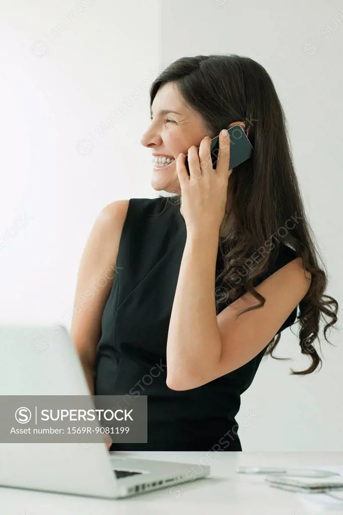 Woman talking on cell phone while using laptop computer