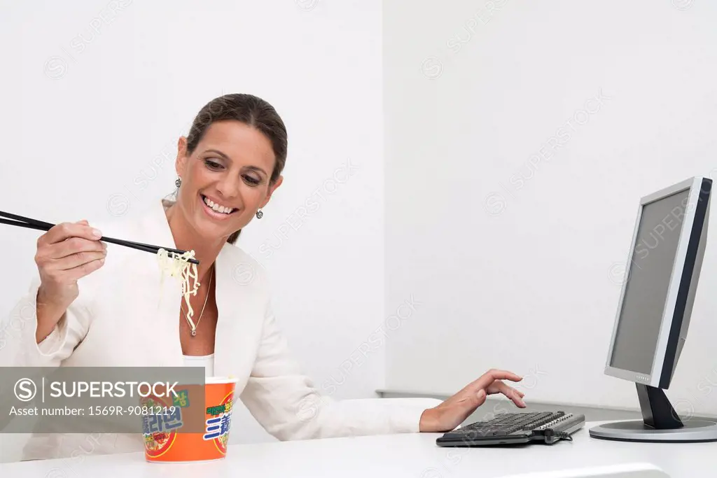 Mature businesswoman eating instant noodles at desk
