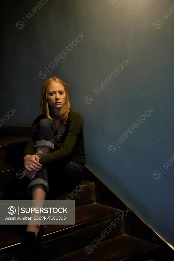 Young woman sitting on stairs, hugging knee