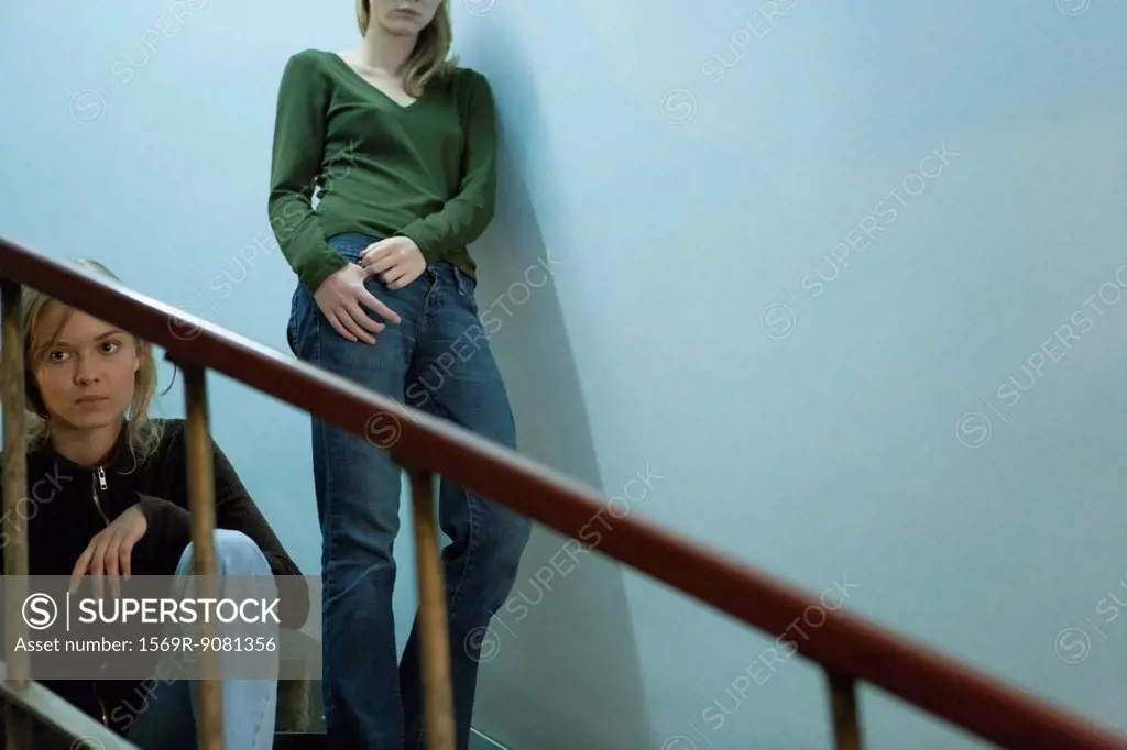 Teen girl sitting on stairs, young woman leaning on wall behind her